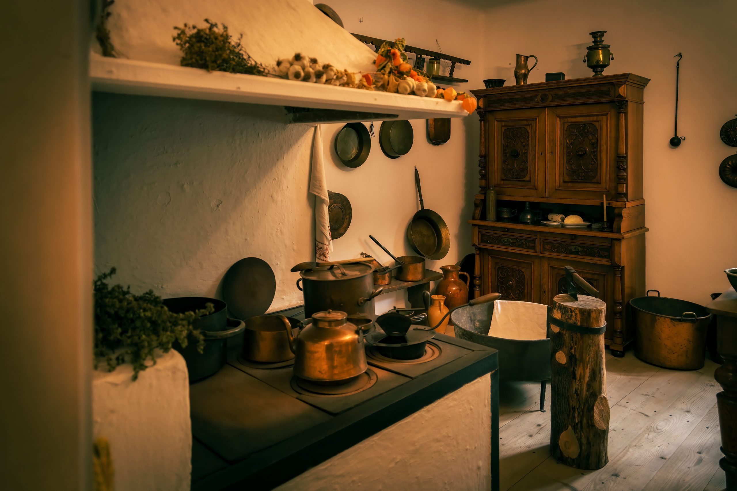 Warm vintage kitchen interior featuring copper kettles, rustic wood furniture, and historical ambiance.